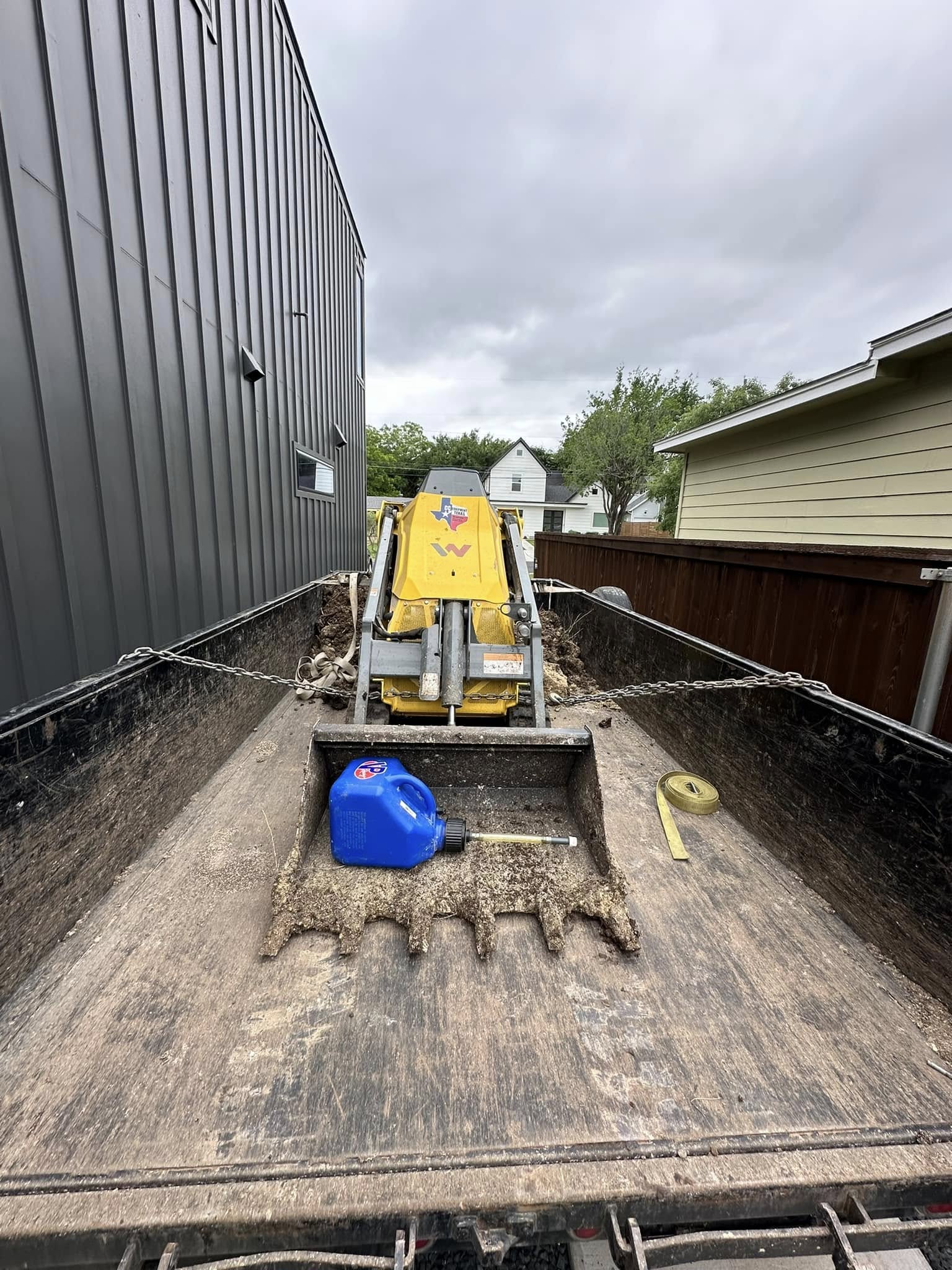 Compact machine on flatbed trailer between buildings